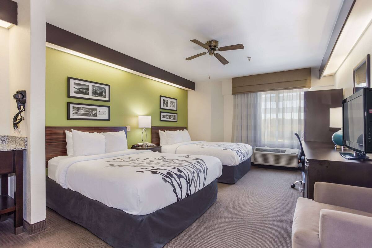 A hotel room with two beds, a desk, a television, and a ceiling fan.
