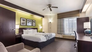 A hotel room with a bed, a desk, a chair, a ceiling fan, a window with curtains, and framed pictures on the wall. - Sleep Inn Little River - North Myrtle Beach (Little River)