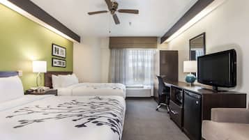 A hotel room with two beds, a ceiling fan, a television, a desk, and a window with curtains.