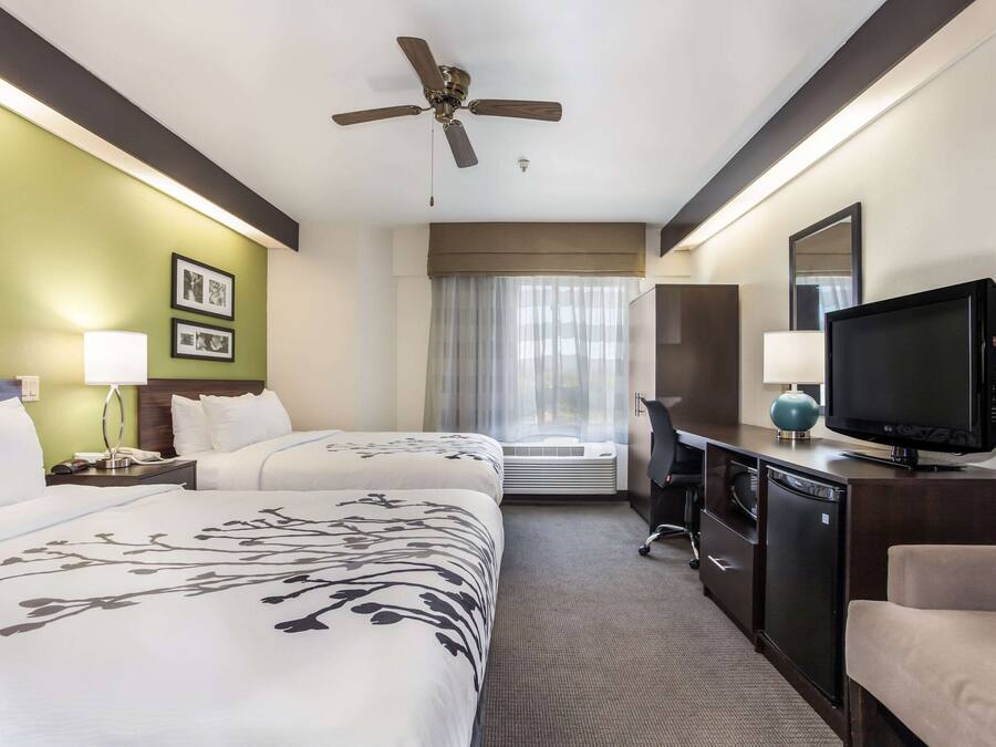 A hotel room with two beds, a ceiling fan, a television, a desk, and a window with curtains.