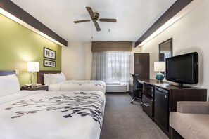 A hotel room with two beds, a ceiling fan, a television, a desk, and a window with curtains.