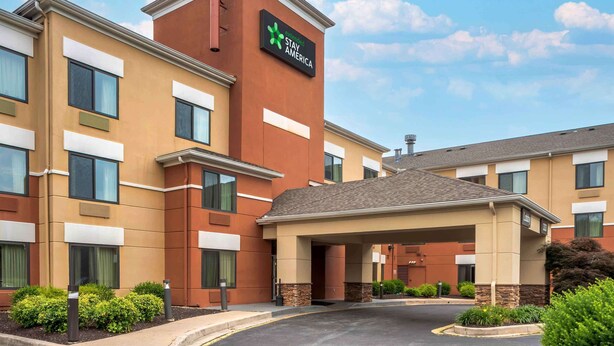 Un hotel Holiday Inn Express con diseño moderno, que cuenta con una entrada central, varios ventanales y un área ajardinada con vegetación.
