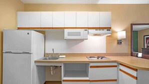 Cocina compacta con gabinetes blancos, microondas, refrigerador y pileta.