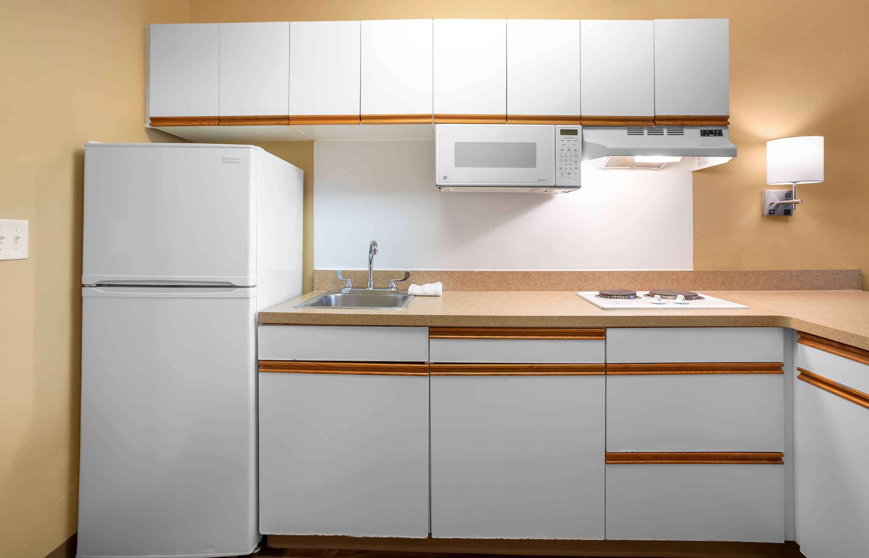 Een kleine keuken met witte kastjes, een magnetron, een spoelbak en een aanrecht.