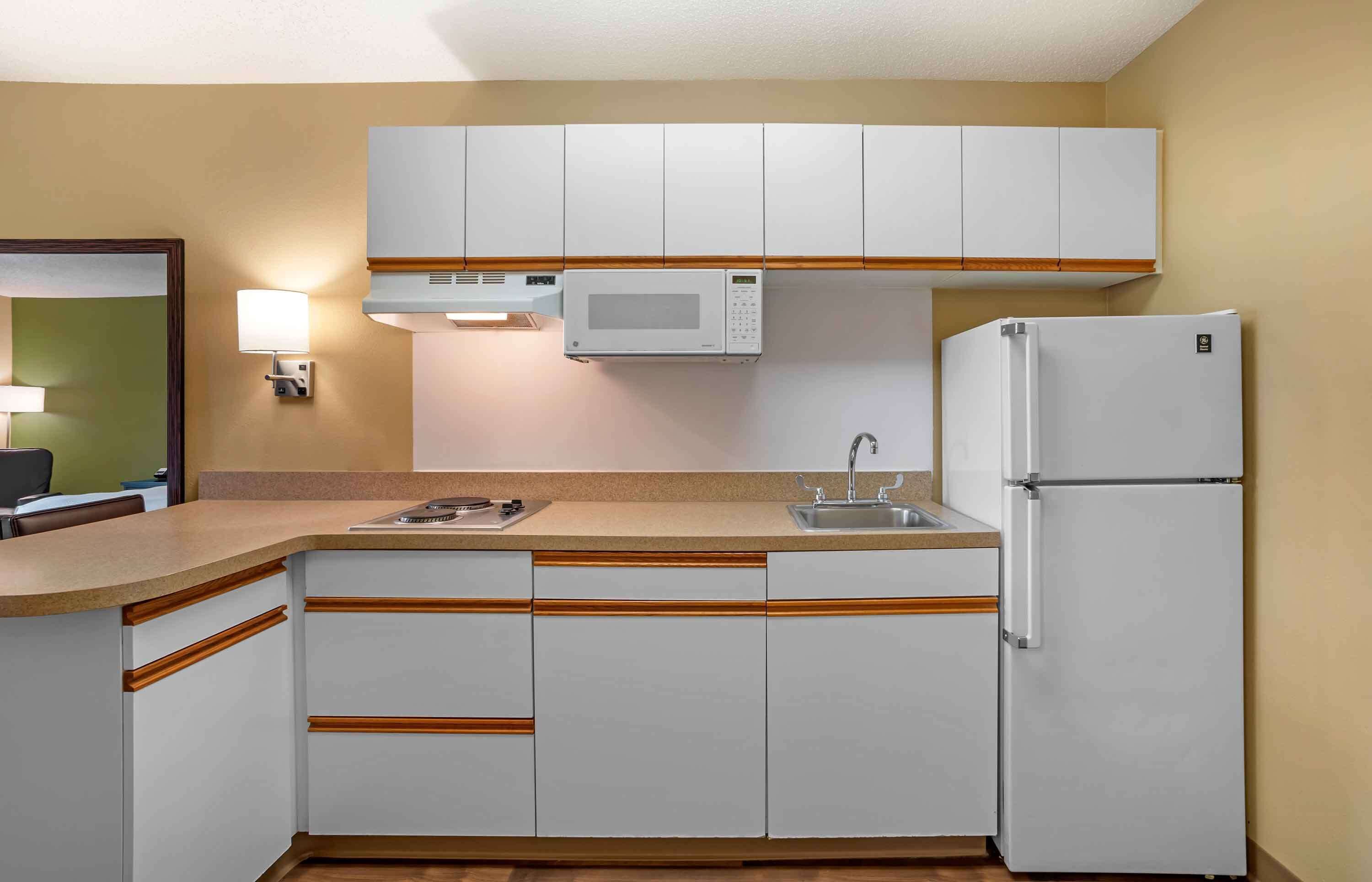 Una cocina compacta con armarios blancos, un microondas, un refrigerador, un lavamanos y una encimera.