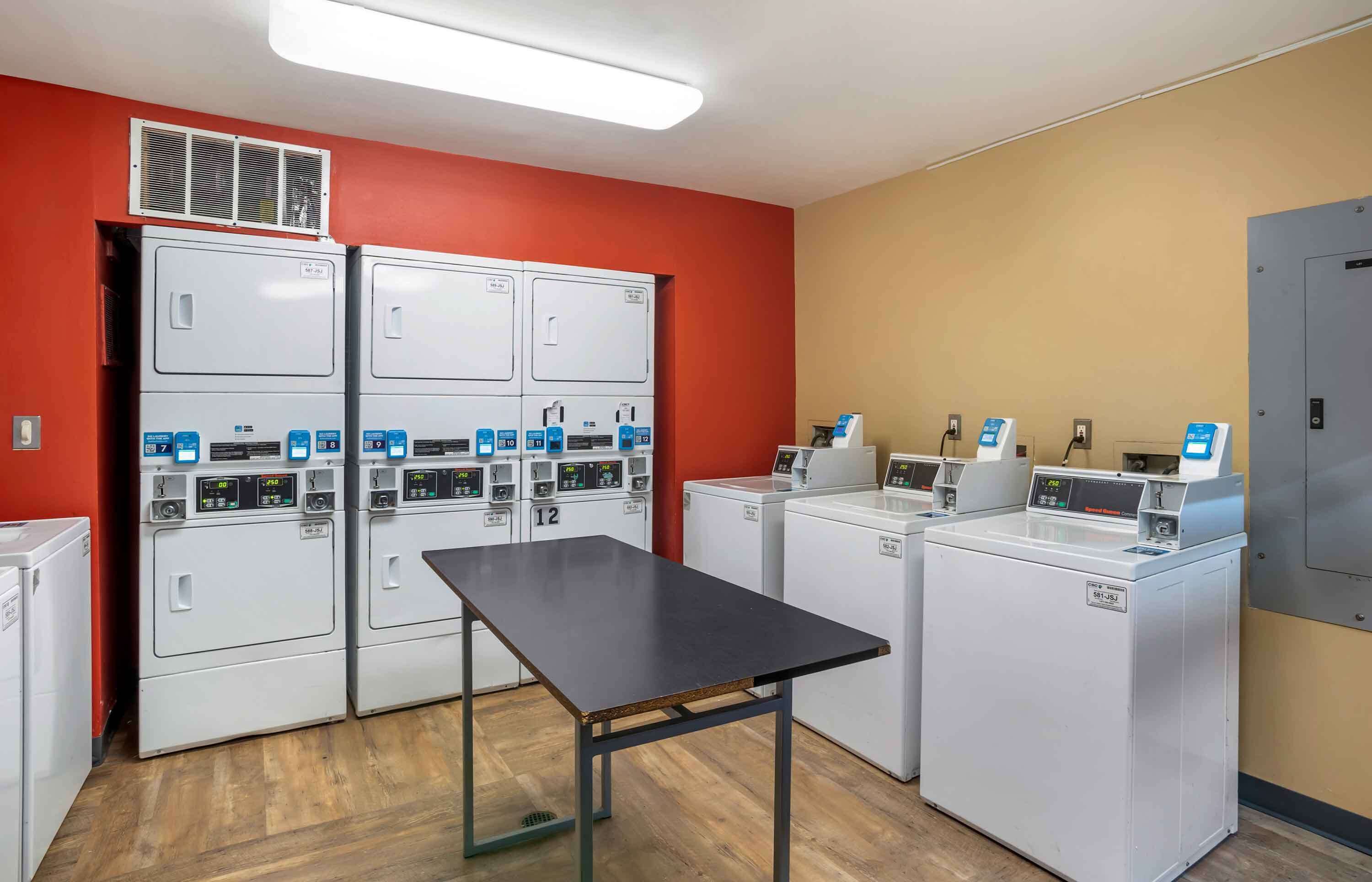 Une buanderie équipée de plusieurs machines à laver, d’une table et d’une bouche d’aération au mur.