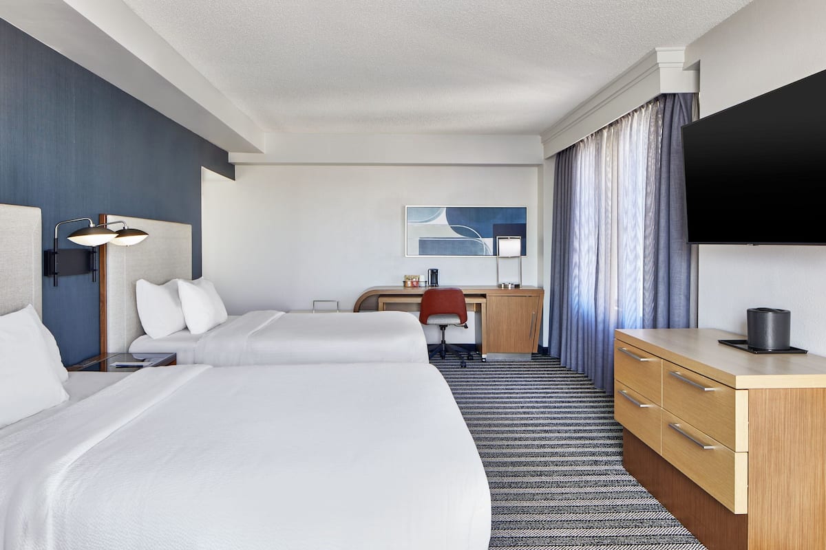 Habitación de hotel con dos camas, un escritorio, una silla, un televisor y un minibar.