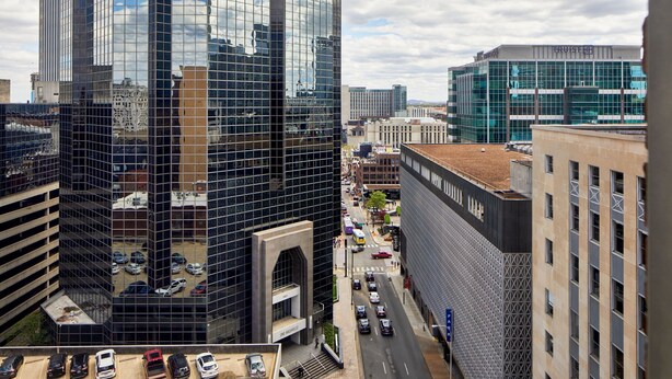 A high-rise building with a glass facade, a parking lot, and a street with cars. - Courtyard By Marriott Nashville Downtown (Nashville)