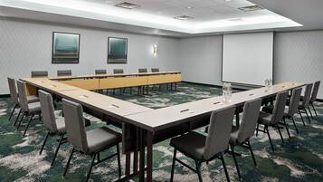 A conference room with a long table, chairs, a projector screen, and a carpeted floor.