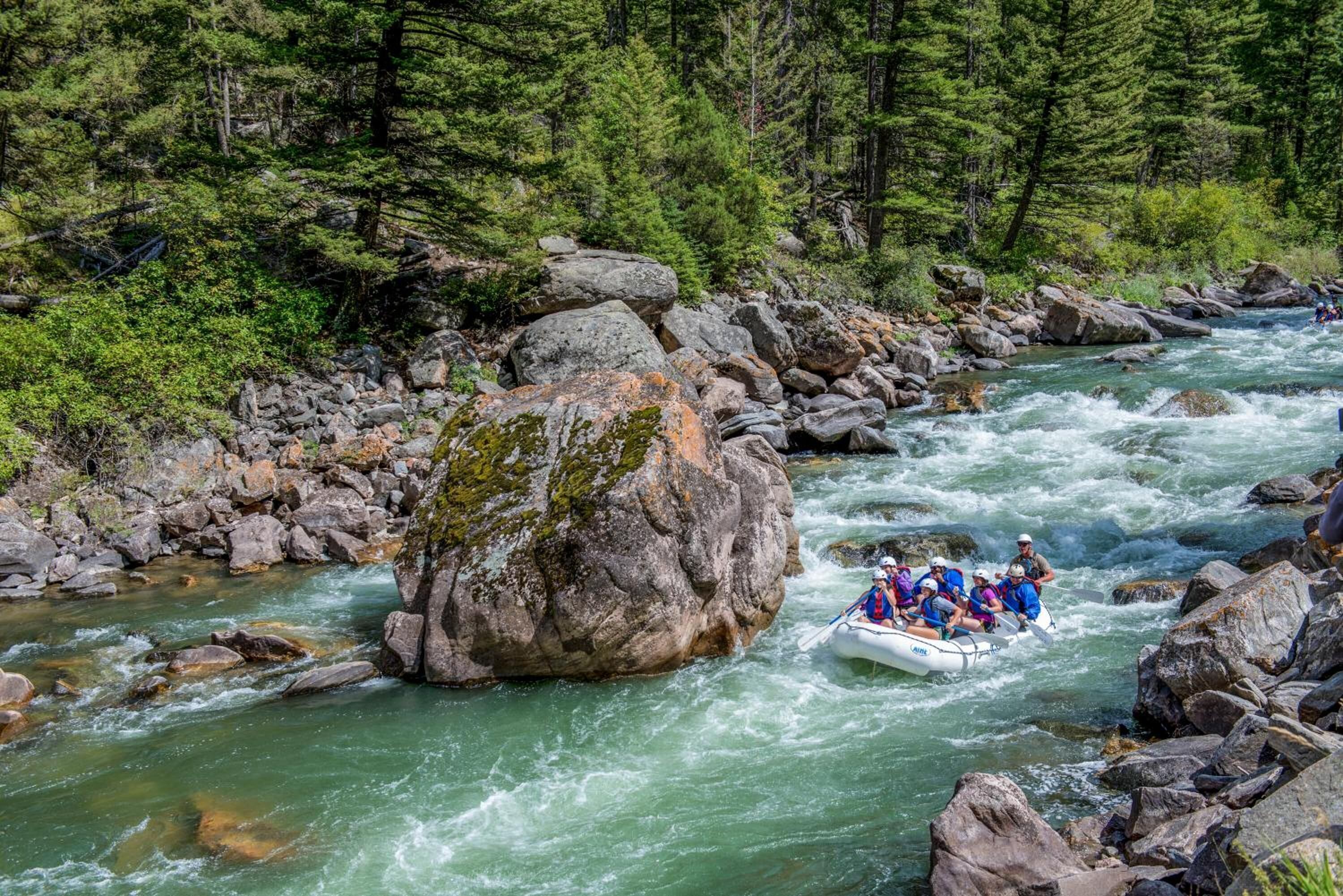 A group of people rafting down a river surrounded by large rocks and dense forest.