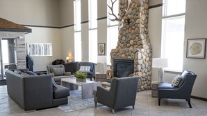 A spacious living room with a stone fireplace, comfortable seating, and large windows. - Whitewater Inn (Gallatin Gateway)
