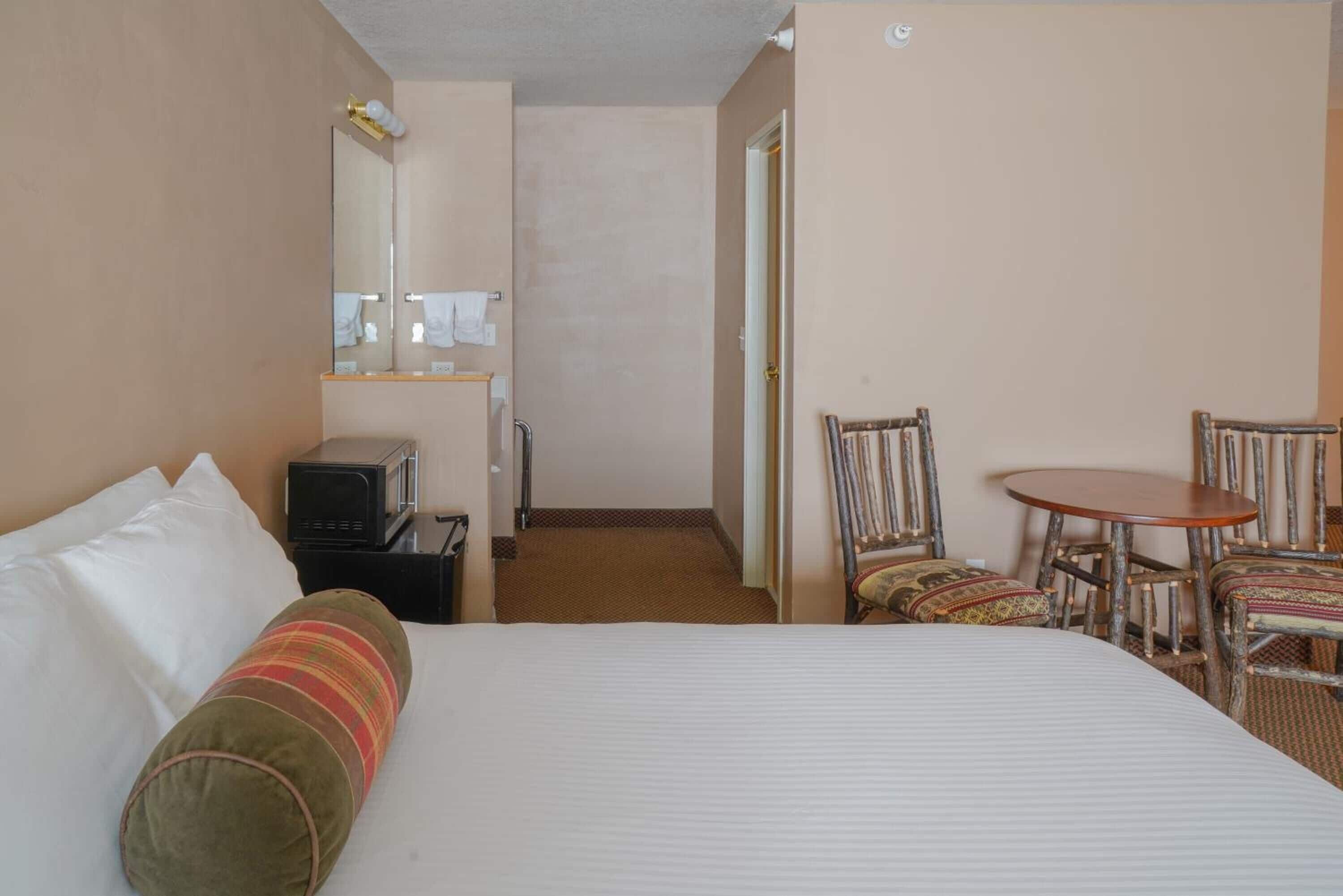 Una habitación de hotel con una cama, un escritorio, una silla, un microondas y un espejo.