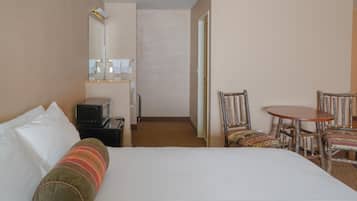 Una habitación de hotel con una cama, un escritorio, una silla, un microondas y un espejo.