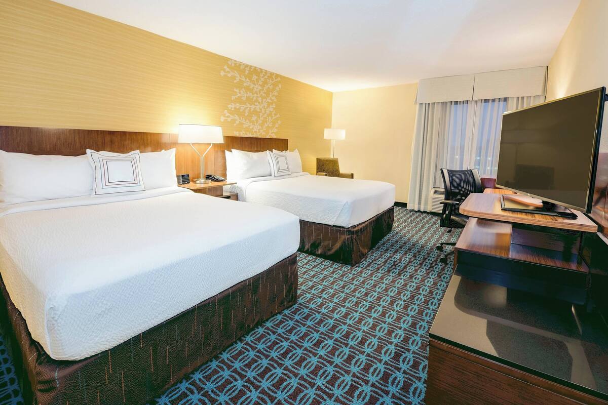 A hotel room with two beds, a desk, a TV, and a patterned carpet.
