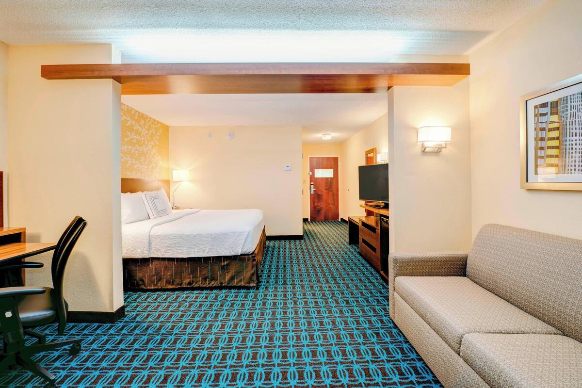 A hotel room with a bed, a sofa, a desk, and a TV.