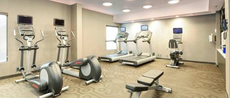 Een fitnessruimte met loopbanden, elliptische trainers en een bank.