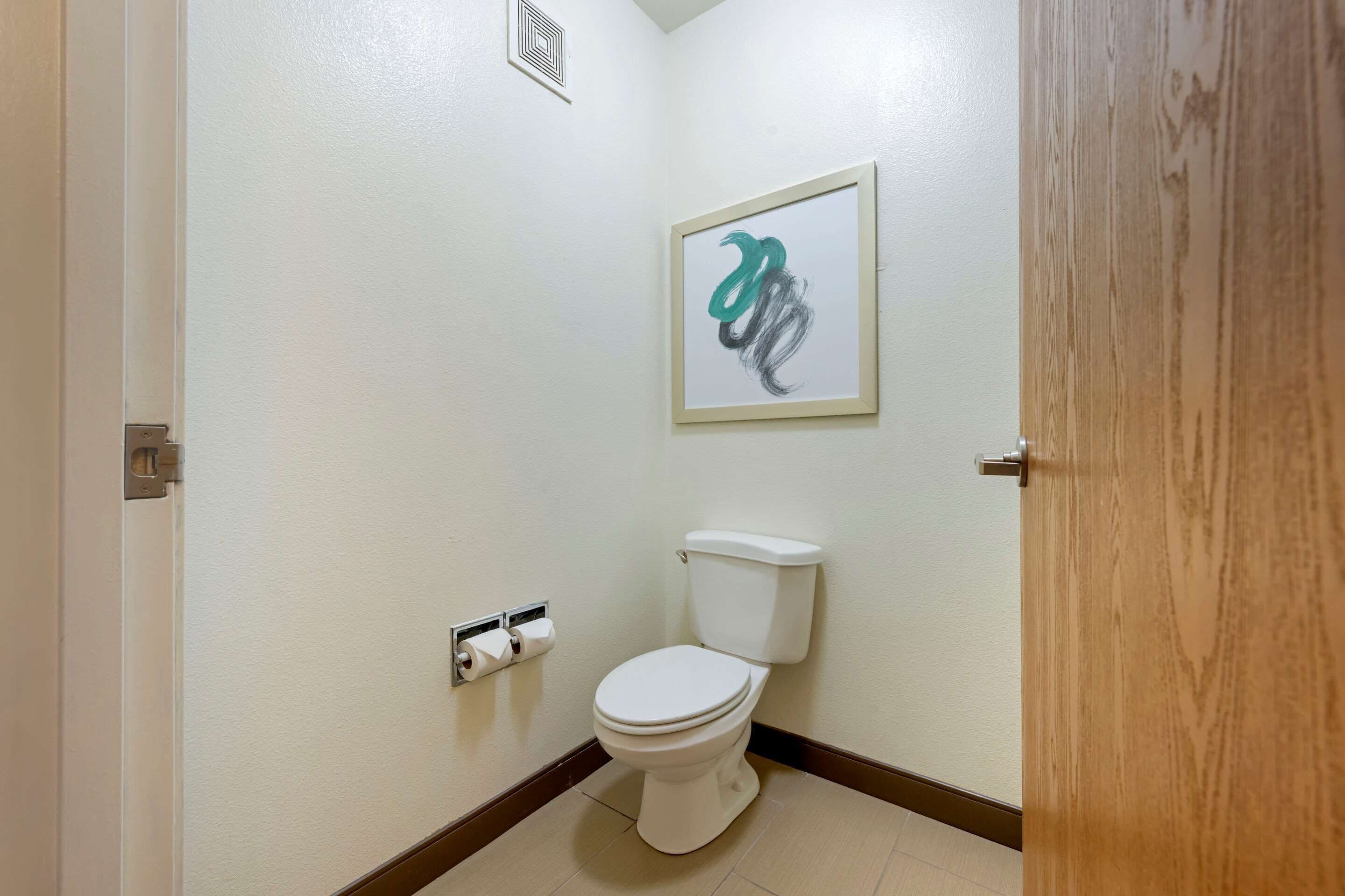 A small, clean bathroom with a white toilet, a framed abstract art piece on the wall, and a toilet paper holder.