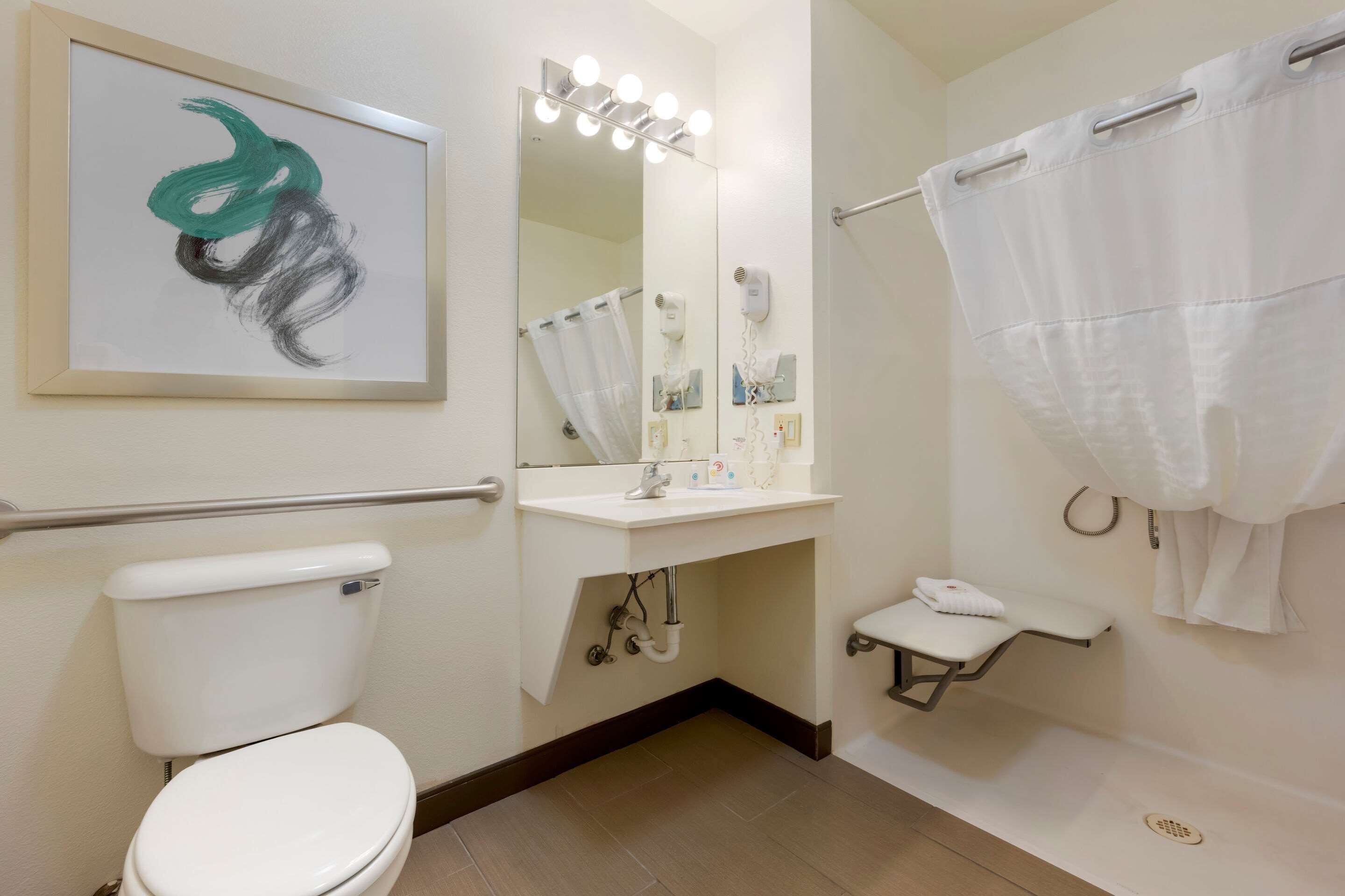 A bathroom with a toilet, sink, mirror with lights, and a shower area.