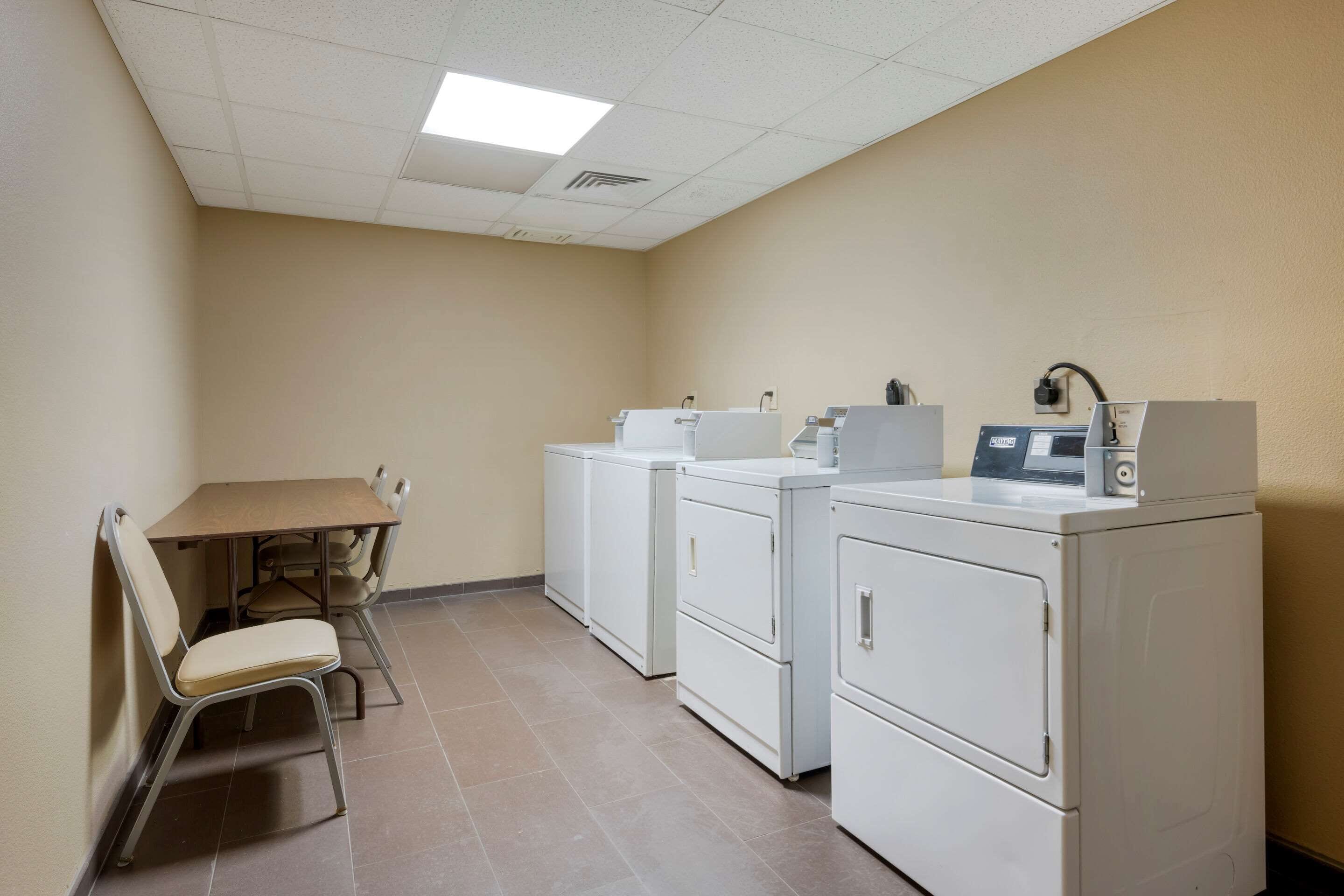 A laundry room with a table and chairs, two washing machines, and a dryer.