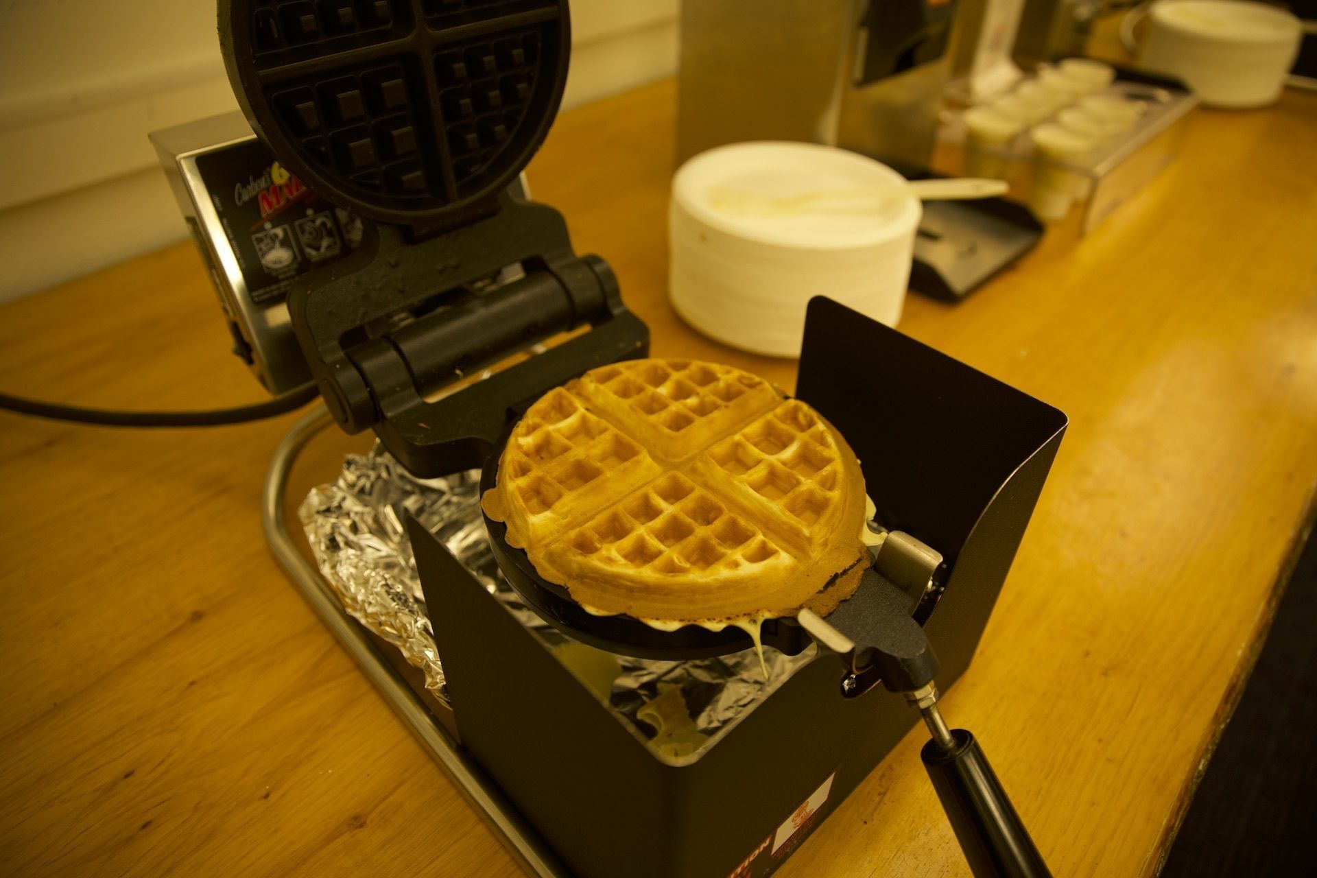 Een wafelijzer met een wafel op een houten ondergrond.