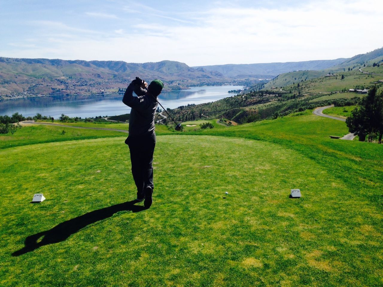 A person playing golf on a lush green field with a scenic view of hills and a lake in the background.