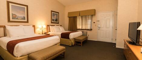 A hotel room with two beds, a television, a desk, and a door.