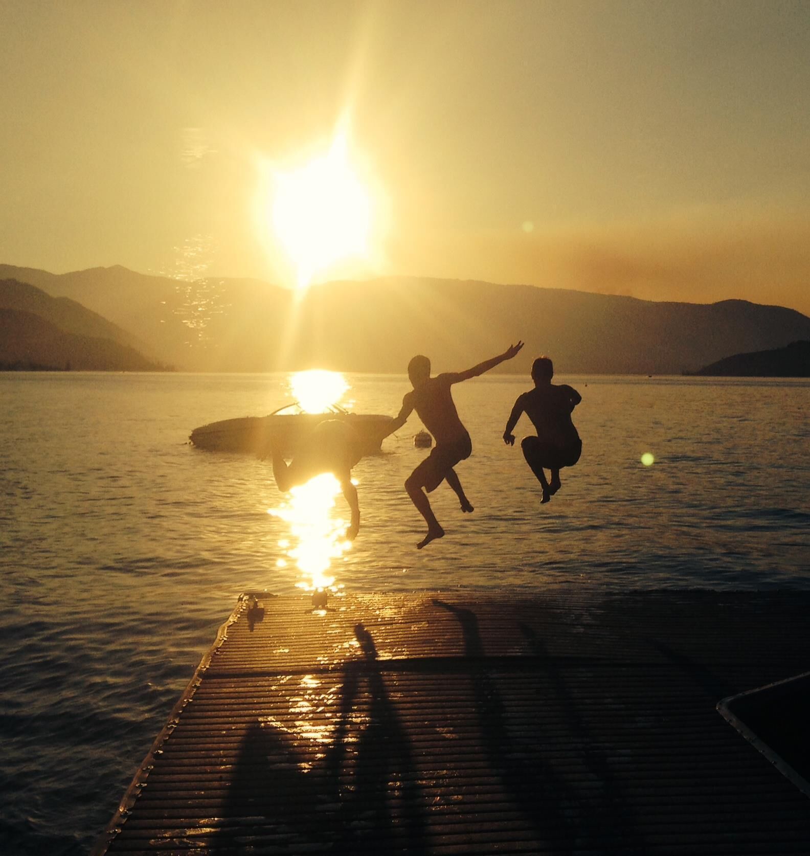 Un tramonto su uno specchio d'acqua con un molo di legno e due figure silhouetate contro il sole.