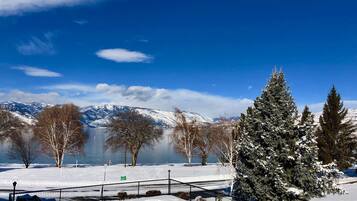 A snow-covered landscape with a clear blue sky, a frozen lake, and snow-covered mountains in the background.