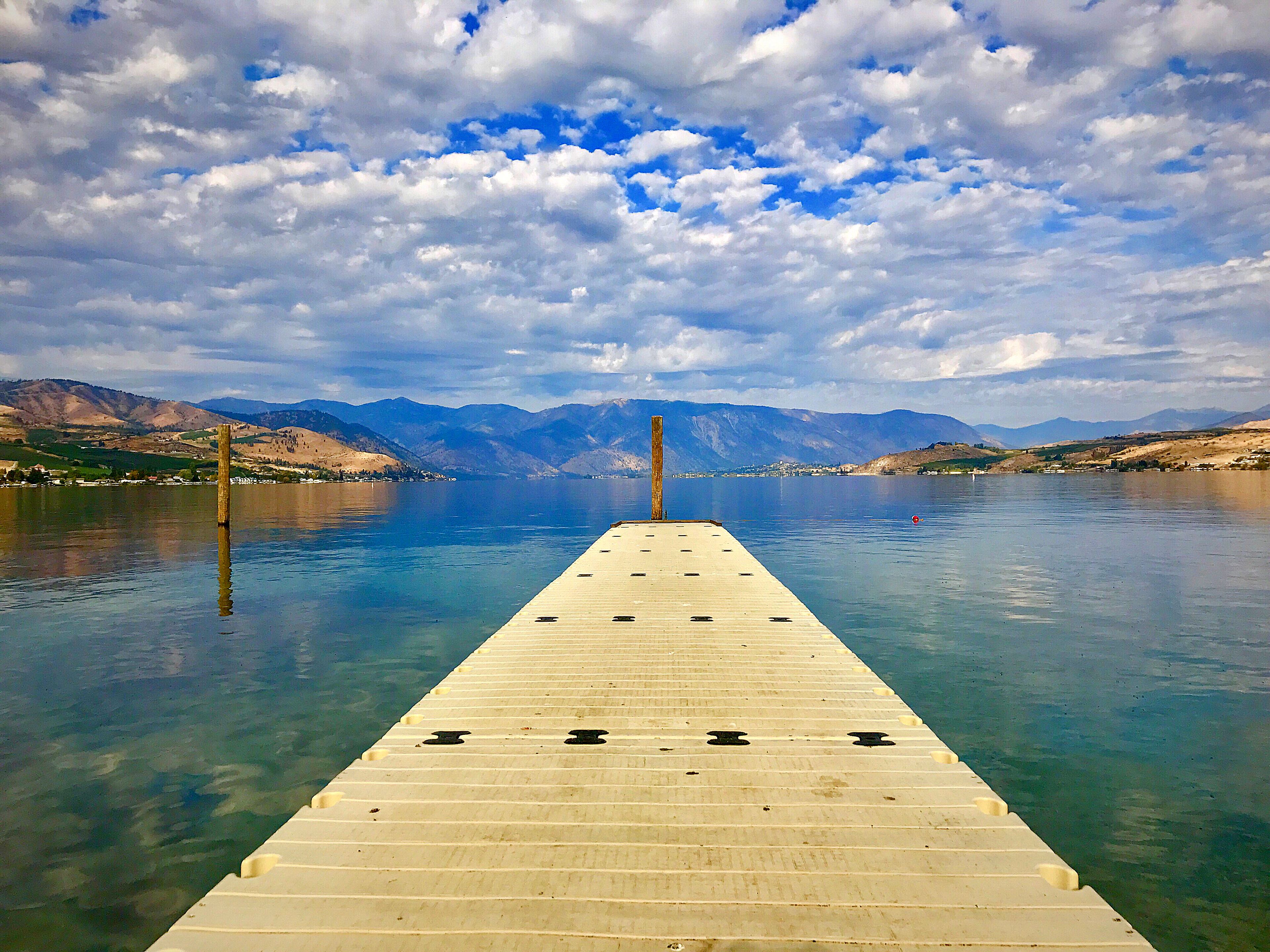 A wooden pier extending into a calm lake with mountains in the background.