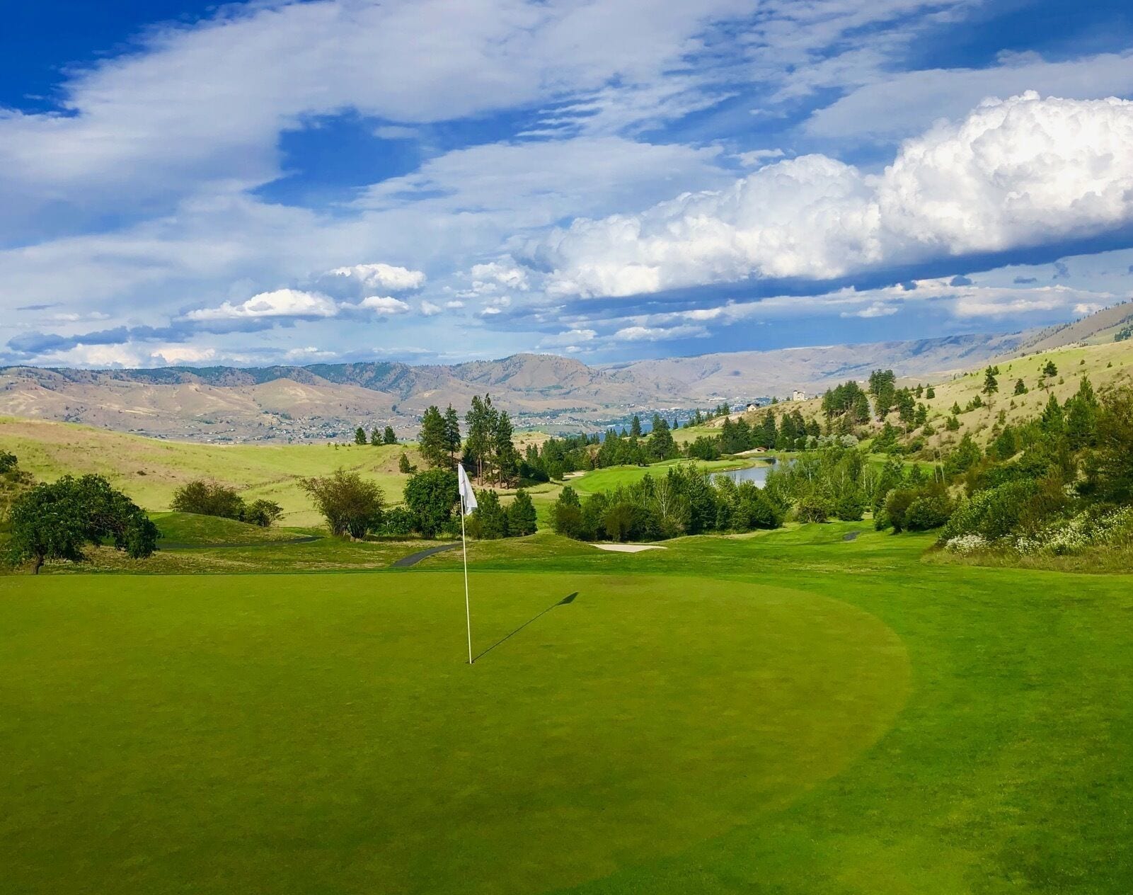 A golf course with a flagstick in the foreground, a lake, and a town in the background.