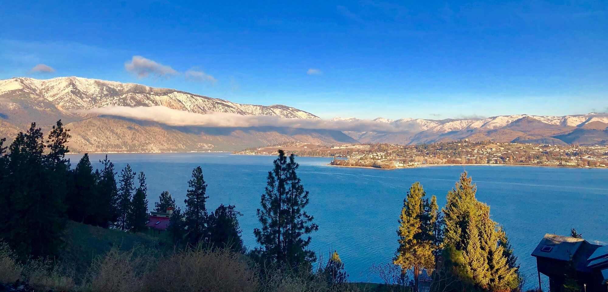 A lake with mountains in the background, surrounded by trees and a small building.