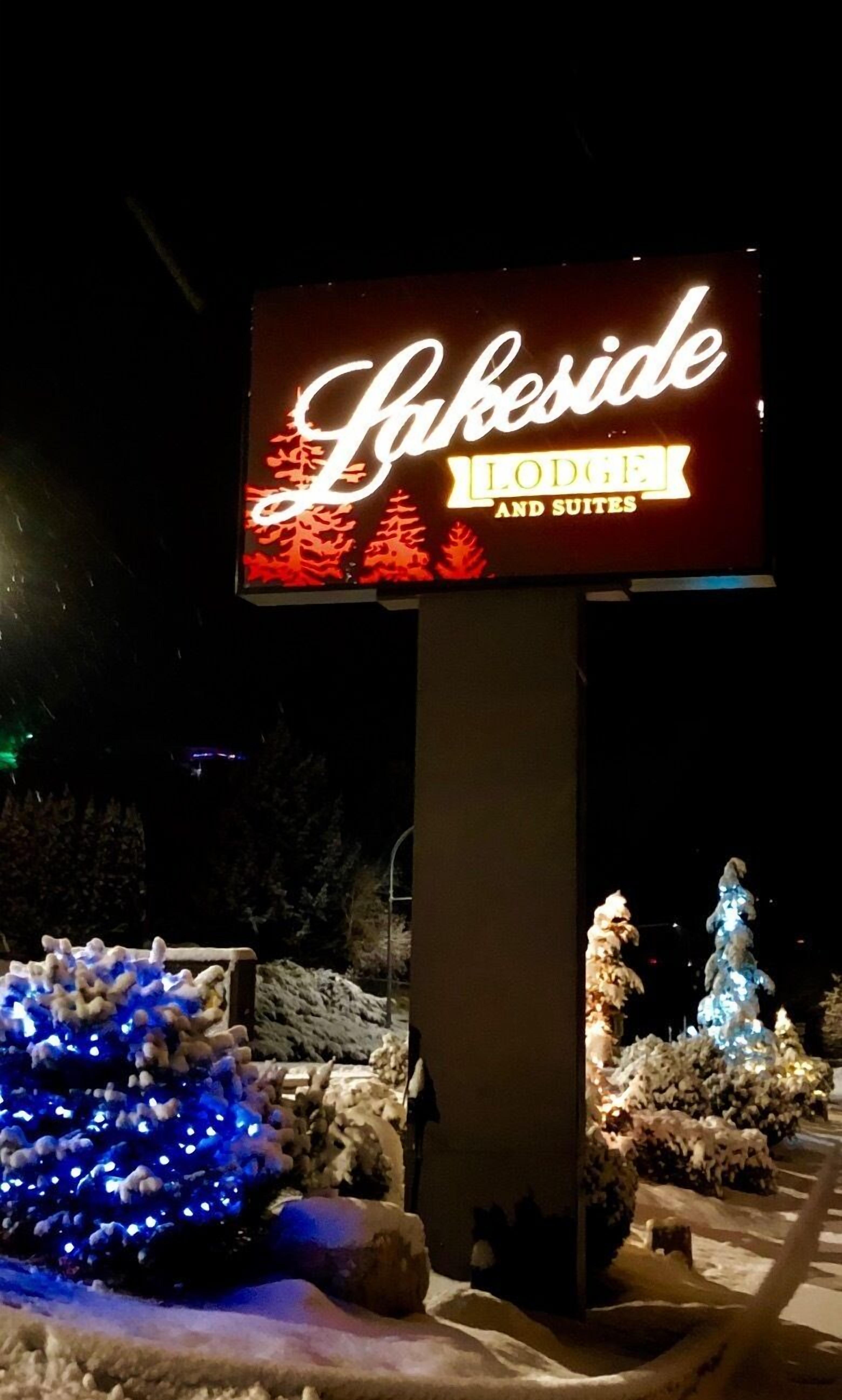A sign for Lakeside Lodge and Suites with illuminated text and a backdrop of trees.