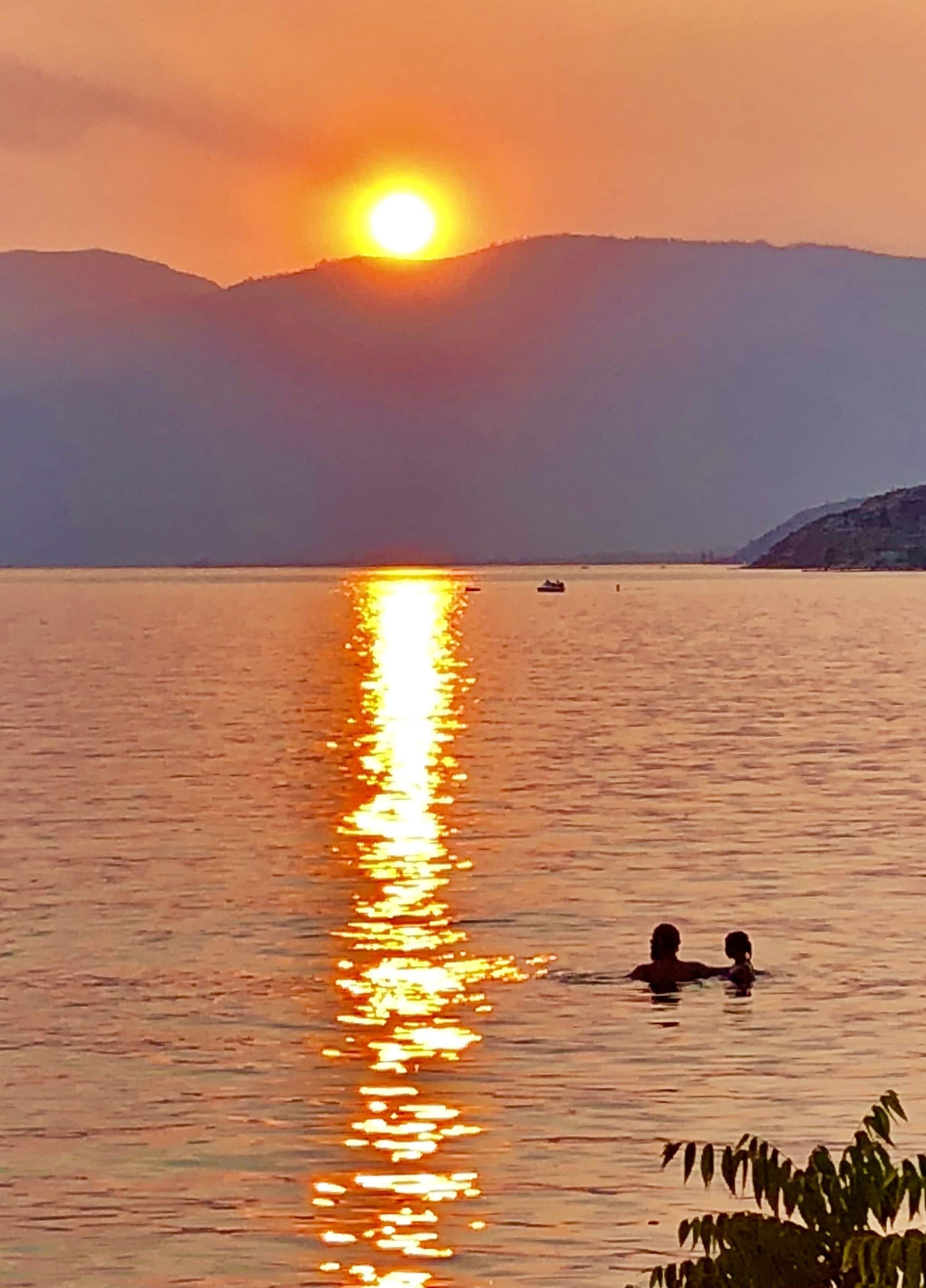 A sunset over a calm body of water with a mountain in the background.