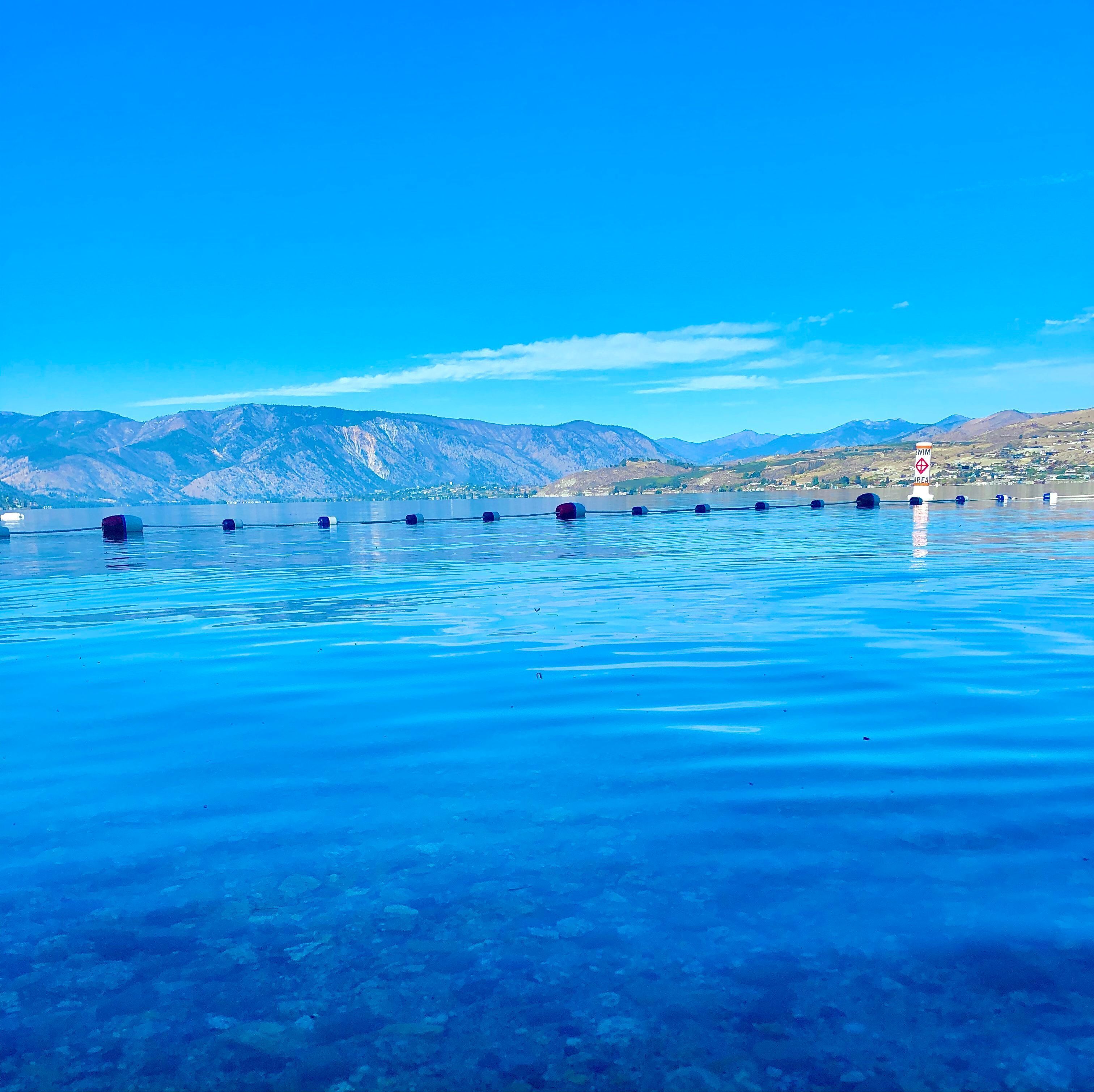 Une piscine d’un bleu éclatant, dotée de bouées et d’un panneau indiquant « baignade interdite », entourée de montagnes et surplombée par un ciel dégagé.