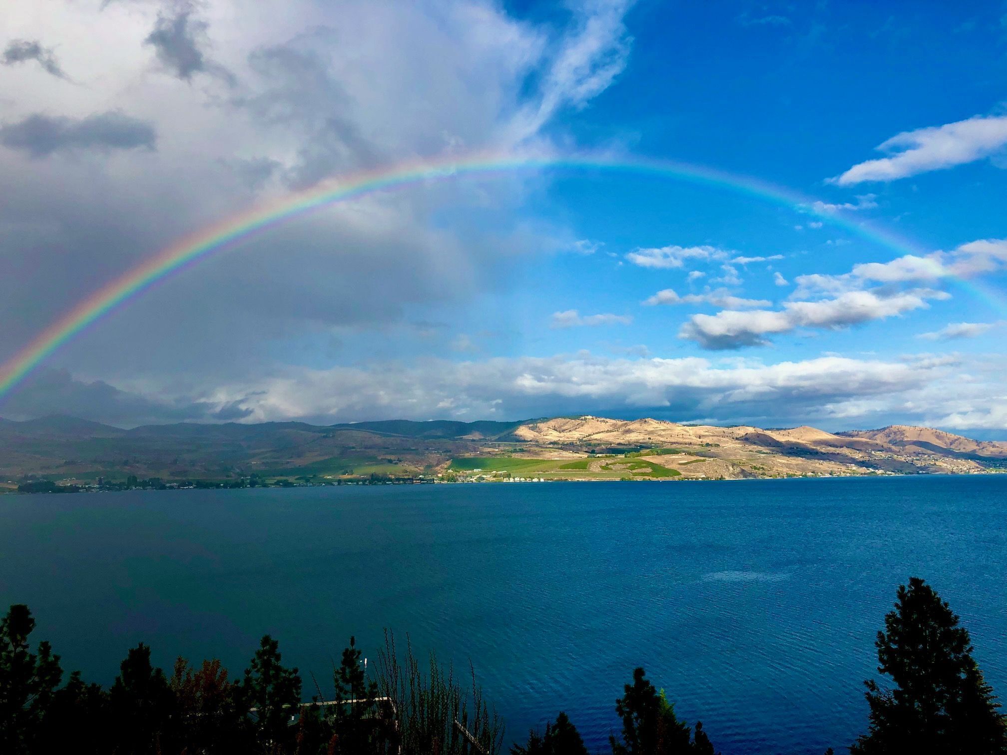 A lake with a rainbow, mountains in the background, and a clear sky.