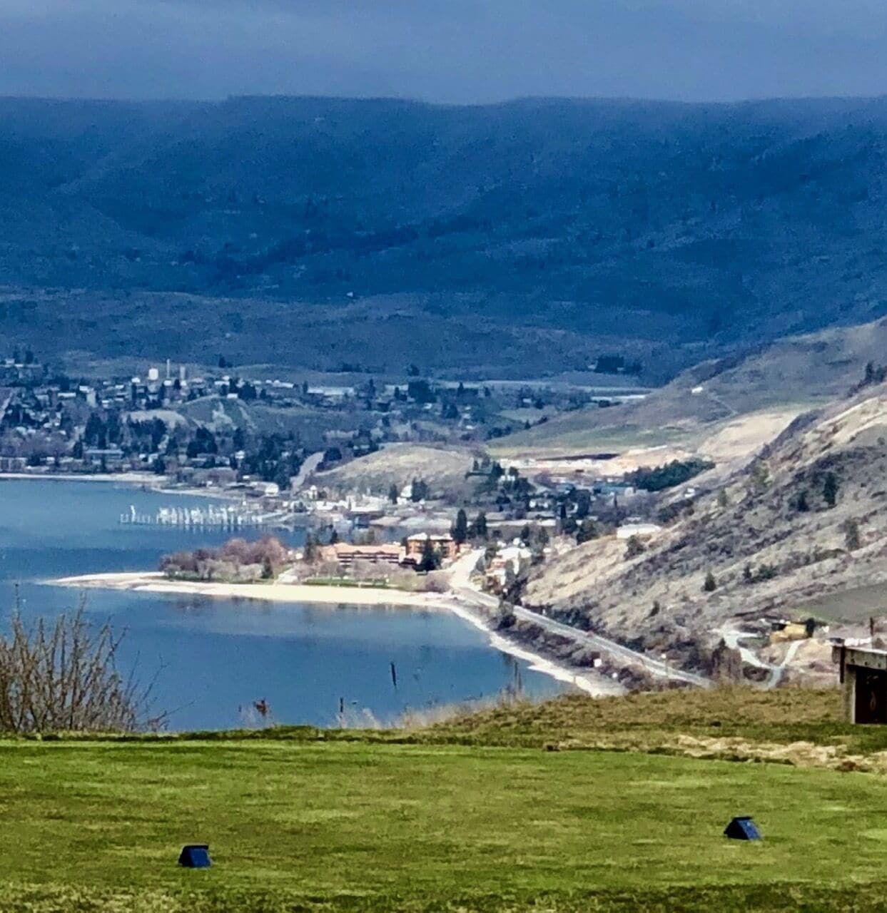 A panoramic view of a coastal town with a lake, hills, and a clear sky.