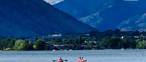 Un lago con kayakistas, rodeado de montañas y un pueblo al fondo.