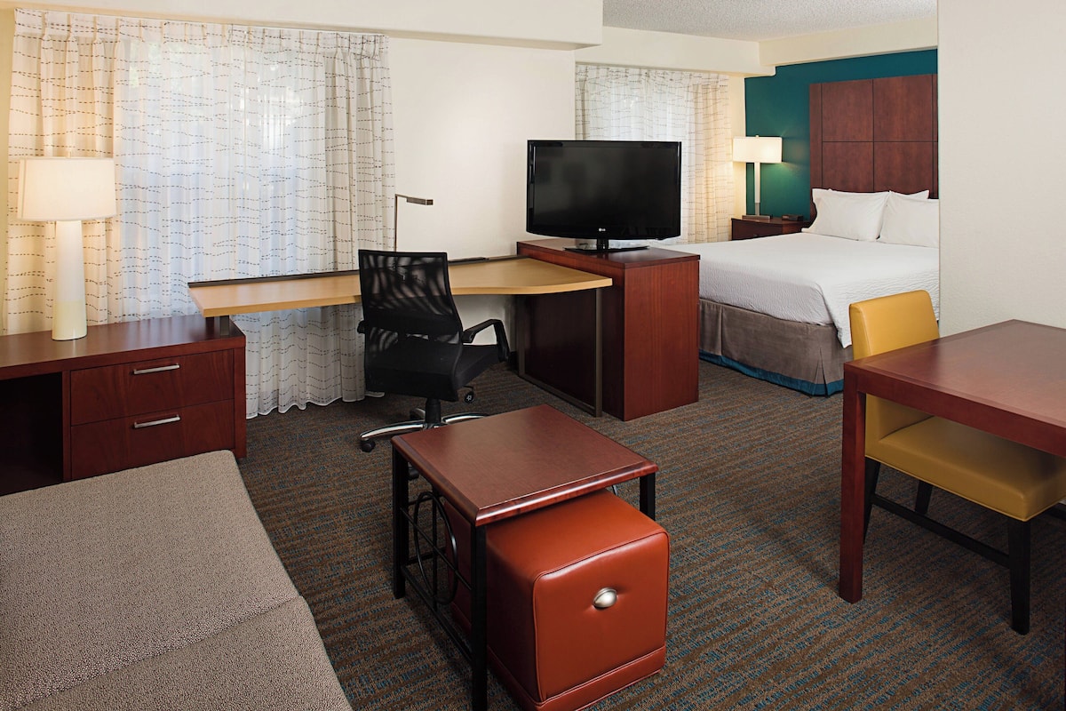 A hotel room with a bed, desk, chair, television, and a small table.