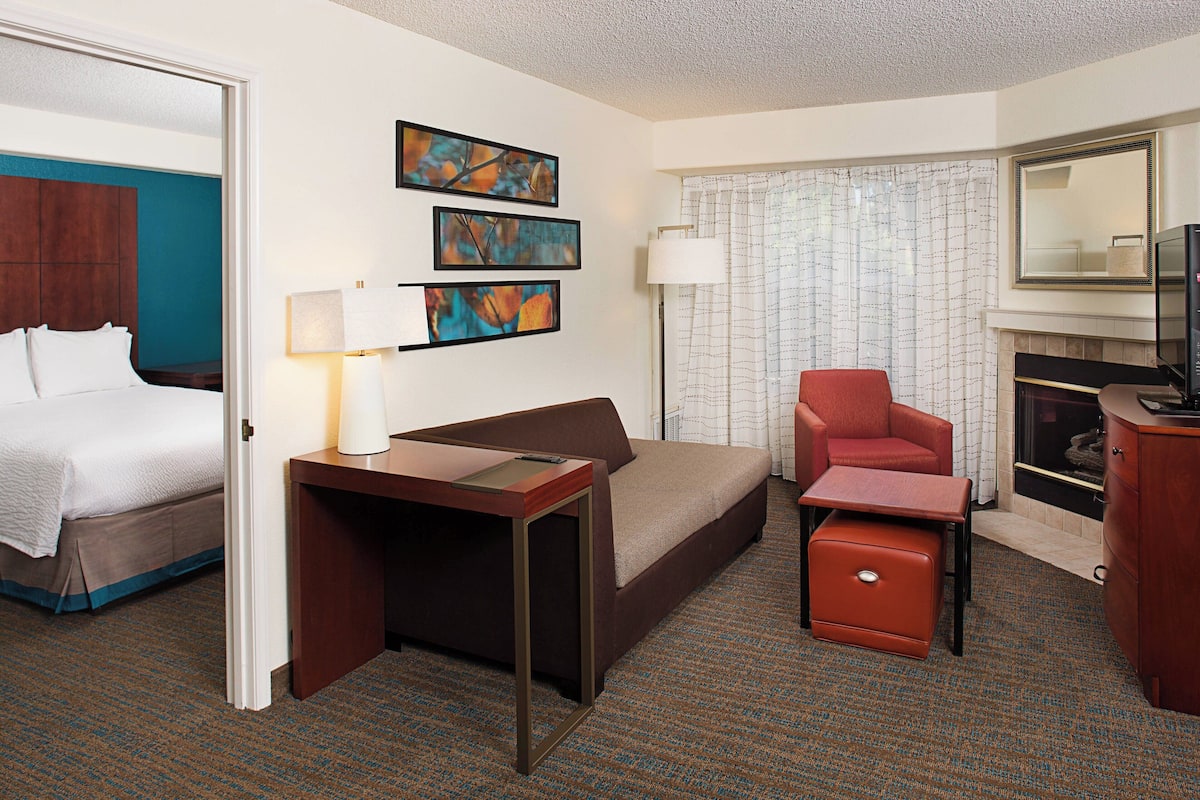 A hotel room with a bed, a sofa, a desk, a chair, a fireplace, and three framed pictures on the wall.