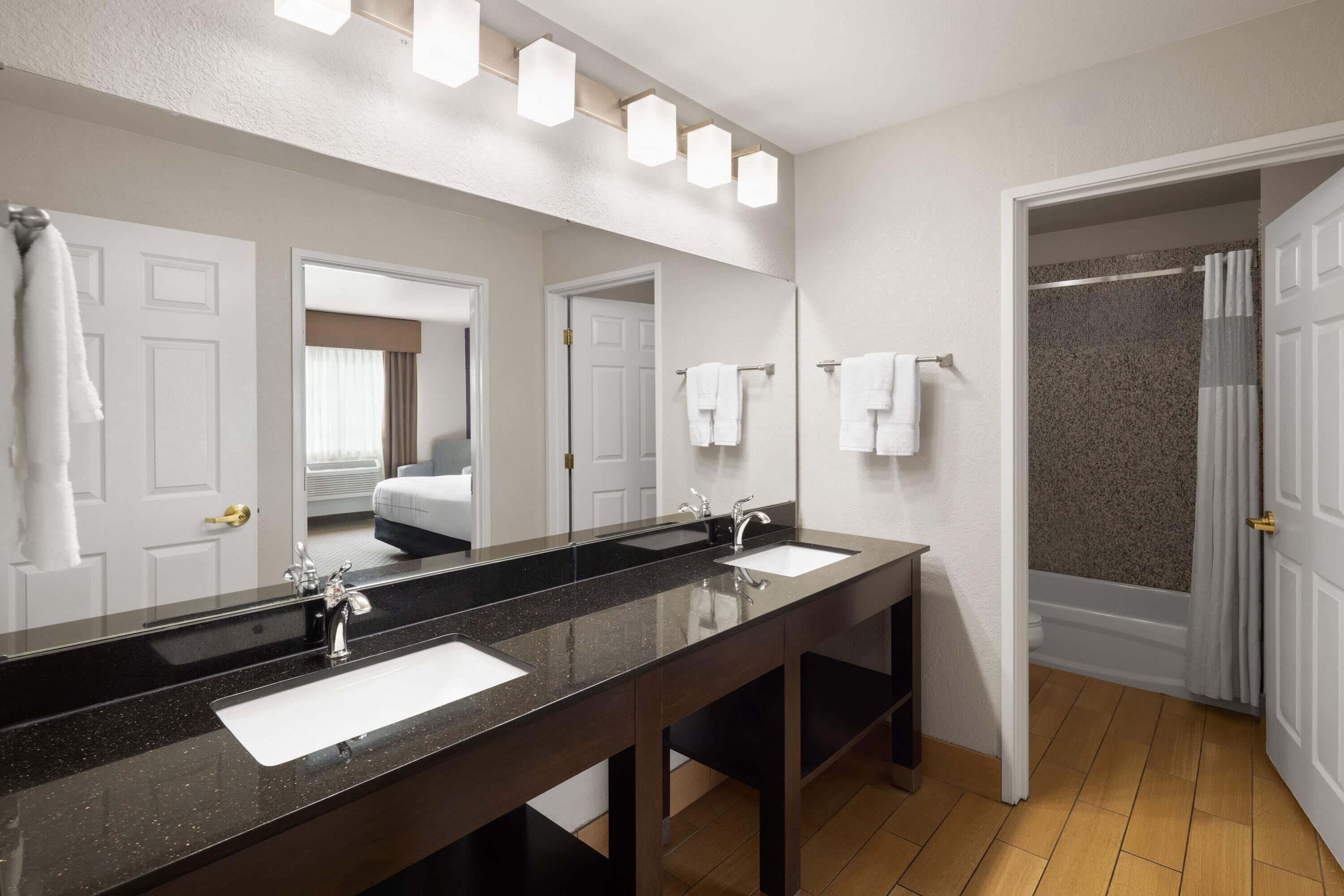 A modern bathroom with a dark granite sink, two mirrors, and a shower area.