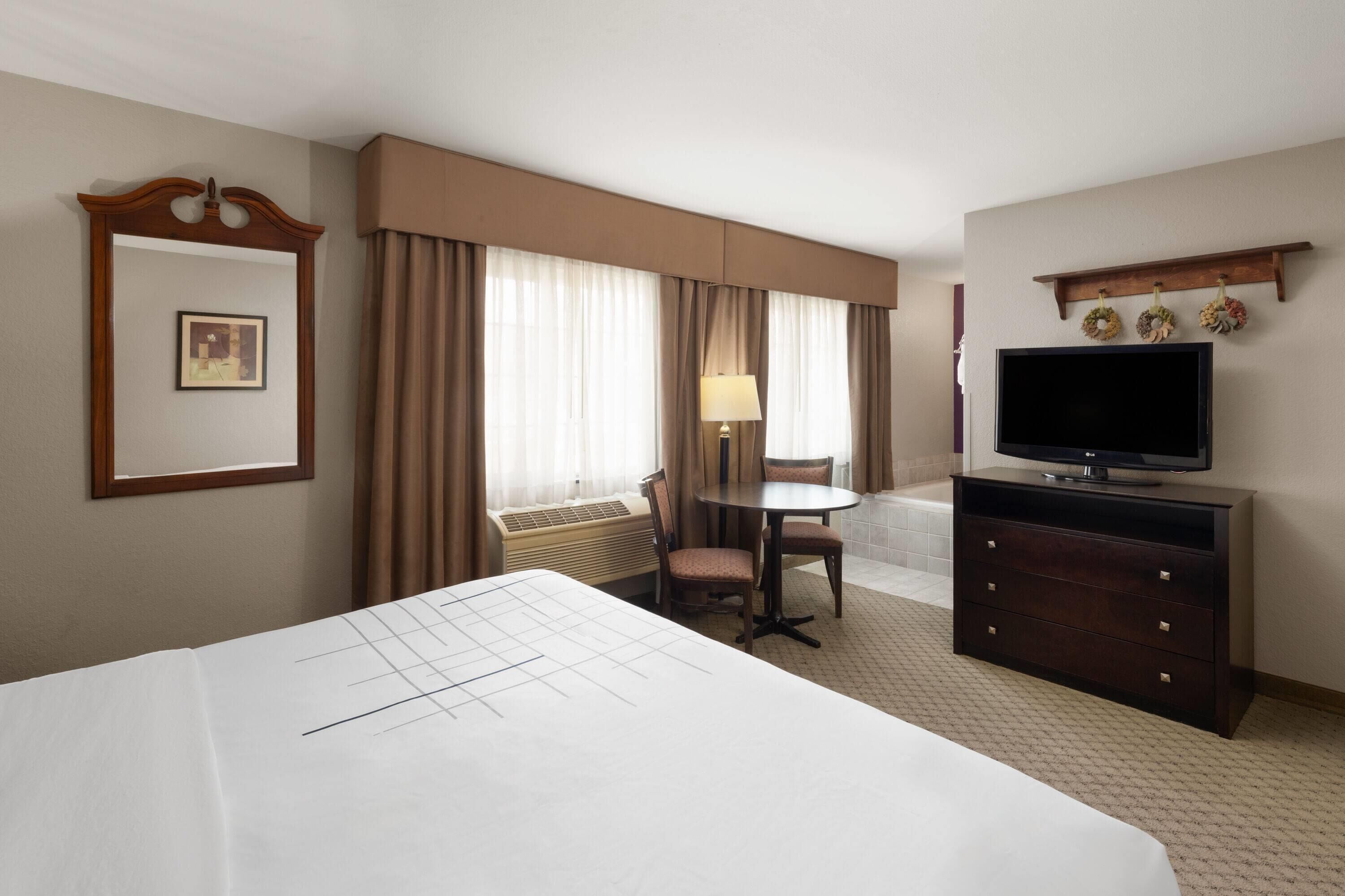 A hotel room with a large bed, a desk with a chair, a television, and a small table with a lamp.