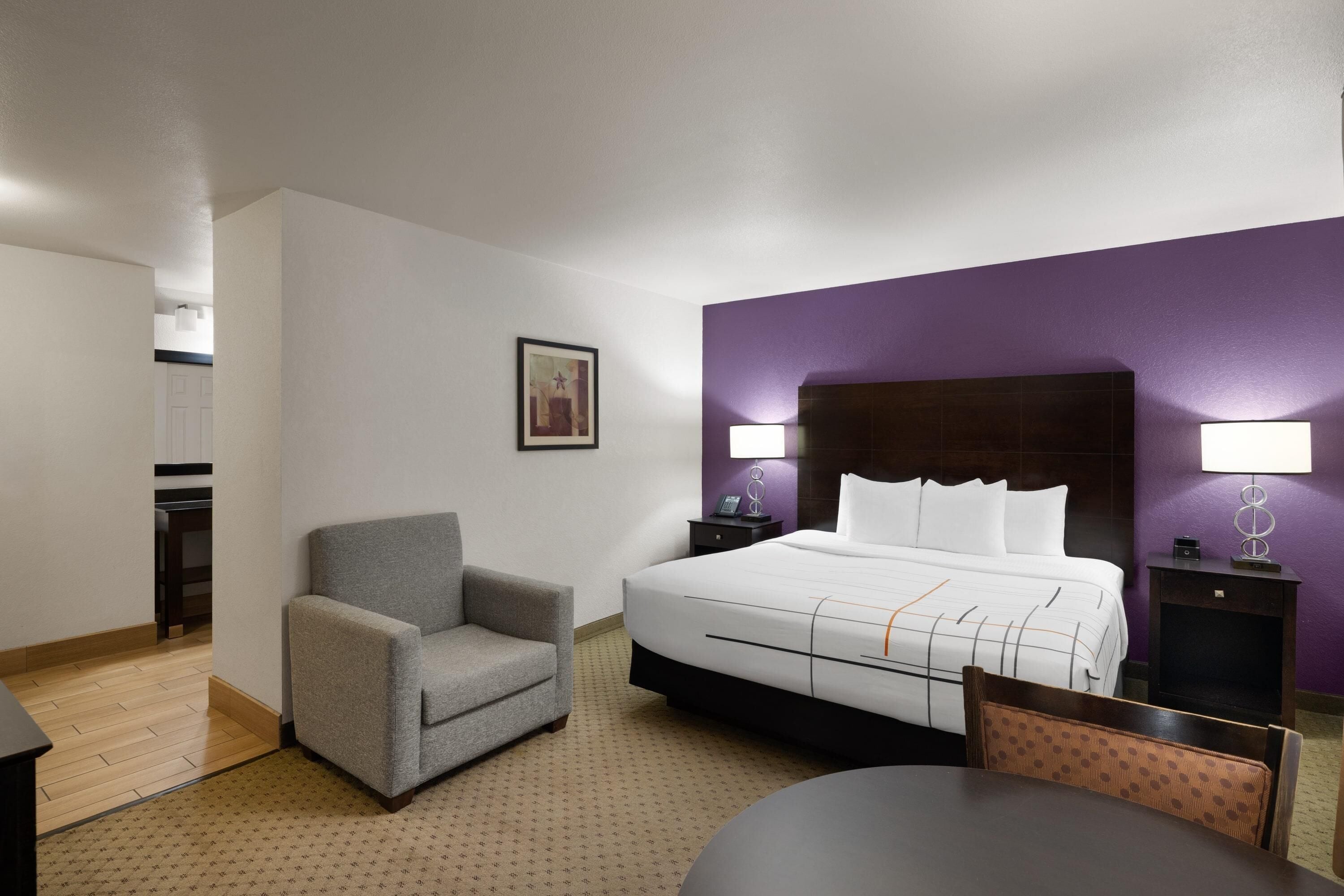 Una habitación de hotel con una cama, una silla, una mesa, una mesita de noche y una lámpara.