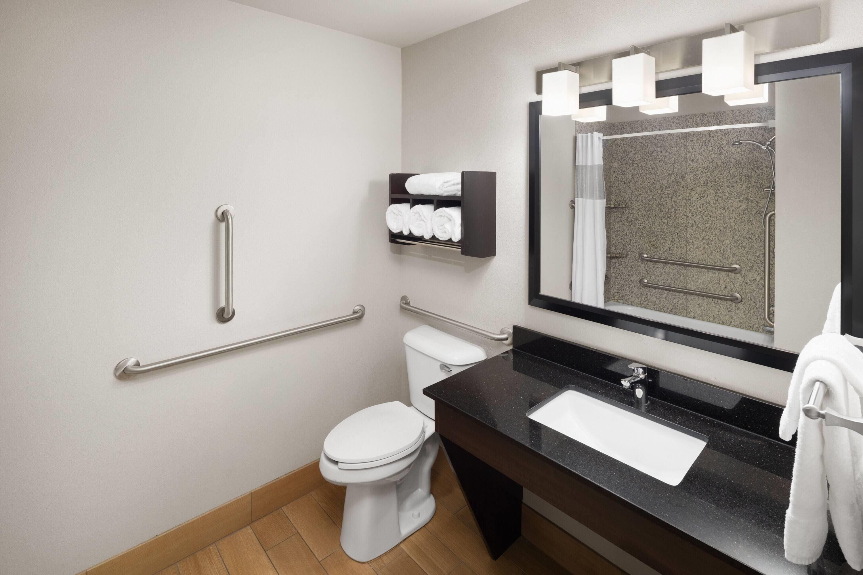 A modern bathroom with a white toilet, a black sink, and a mirror with lights.
