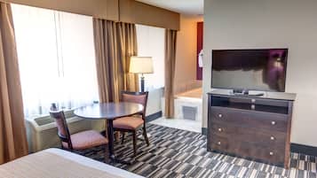 Habitación de hotel con cama, una mesa redonda con sillas, televisor, cómoda y ventana con cortinas.