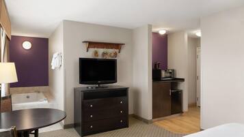 A hotel room with a TV, a small kitchenette, a bathtub, and a dining area.