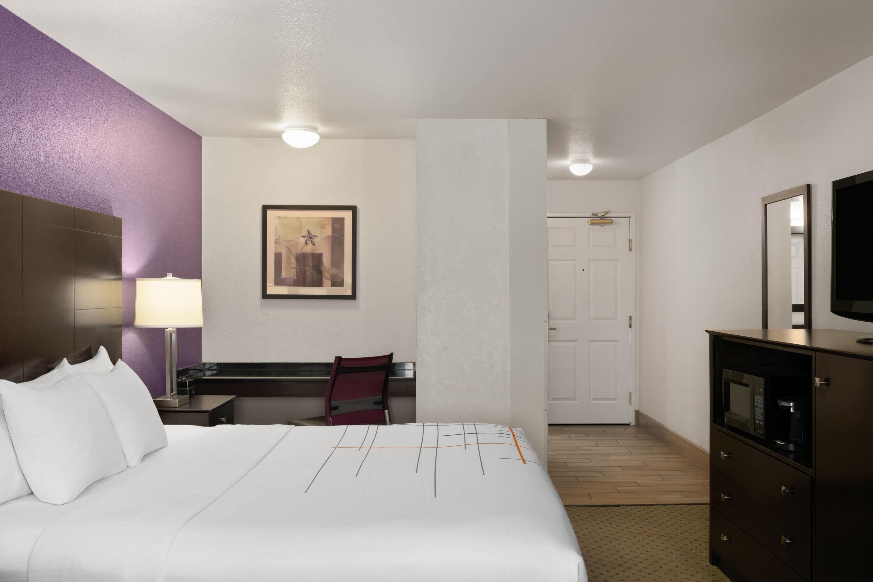 A hotel room with a bed, a desk, a chair, a TV, and a door leading to the bathroom.