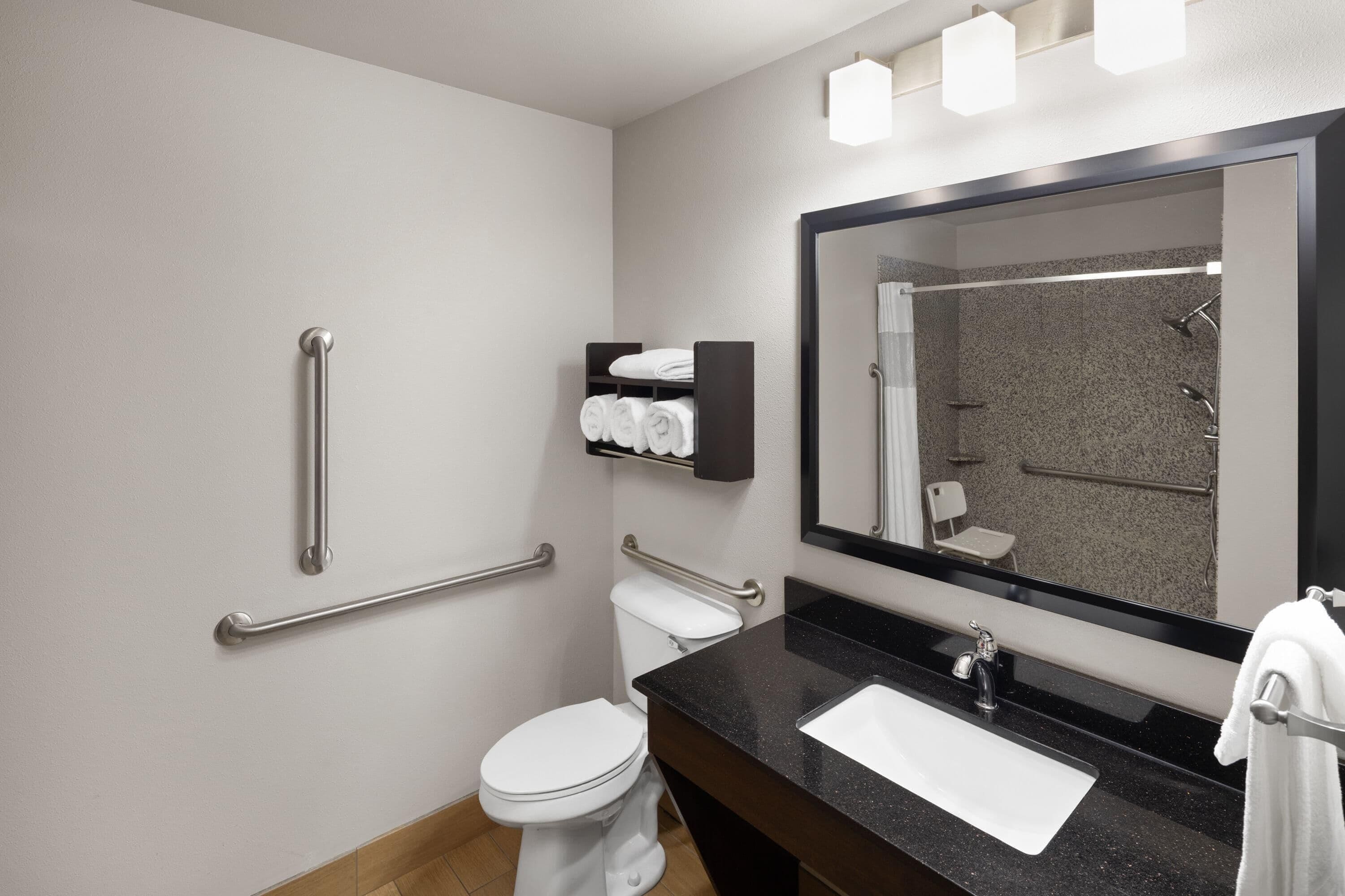 A modern bathroom with a white toilet, a black sink, a large mirror, and a towel rack.