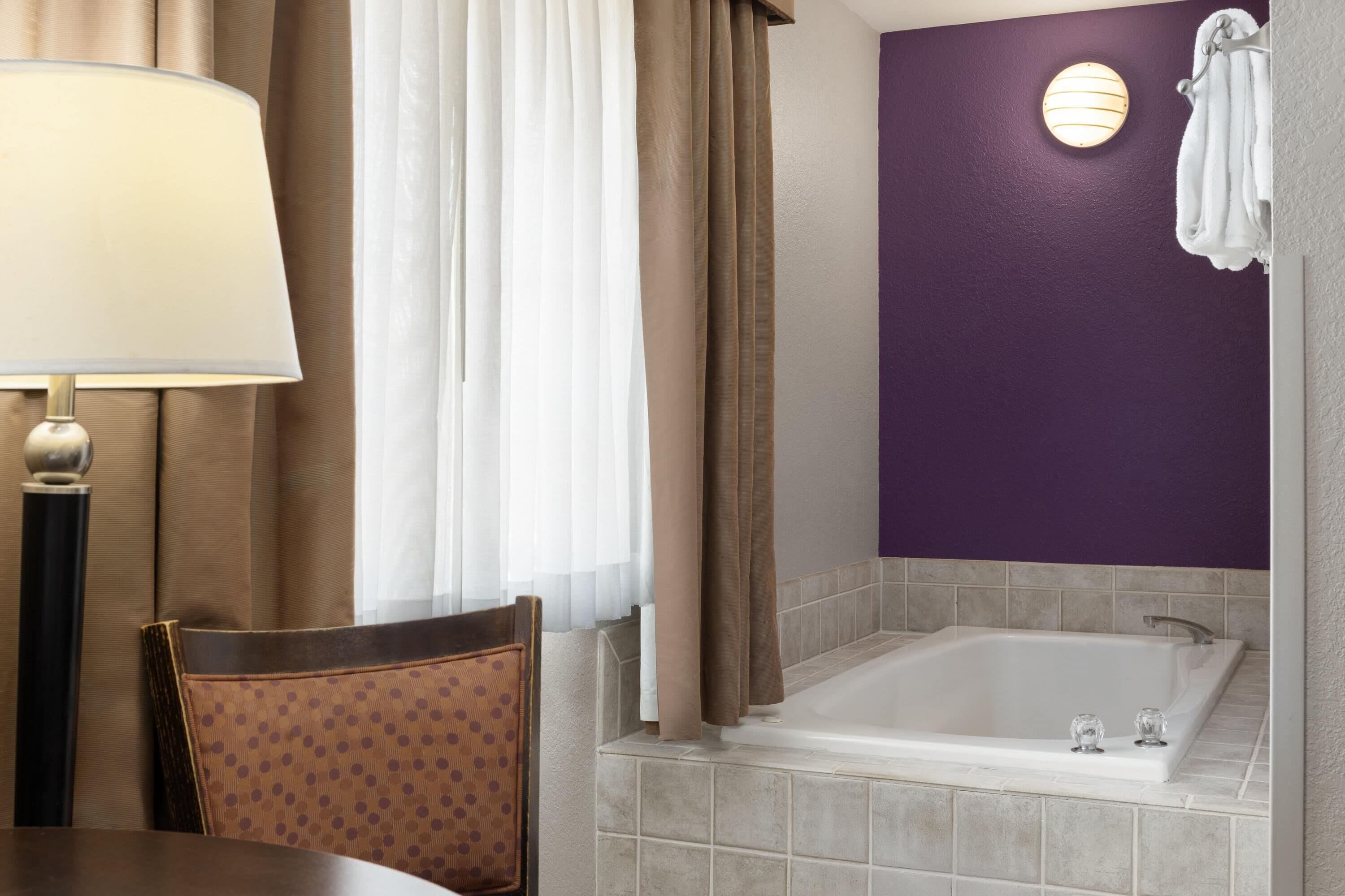 A bathroom with a bathtub, a chair, a table, and a lamp.