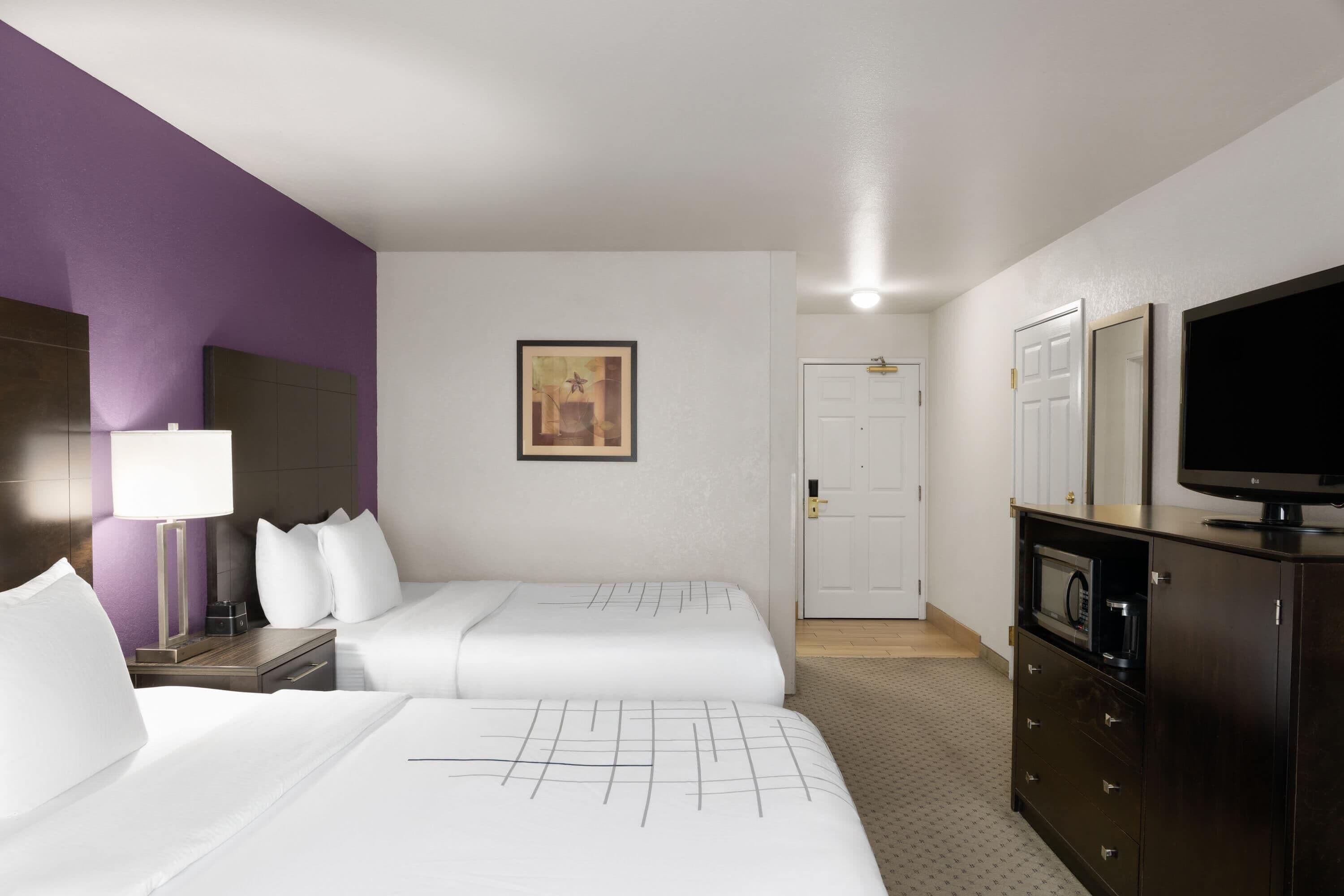 A hotel room with two beds, a TV, a microwave, and a cabinet.