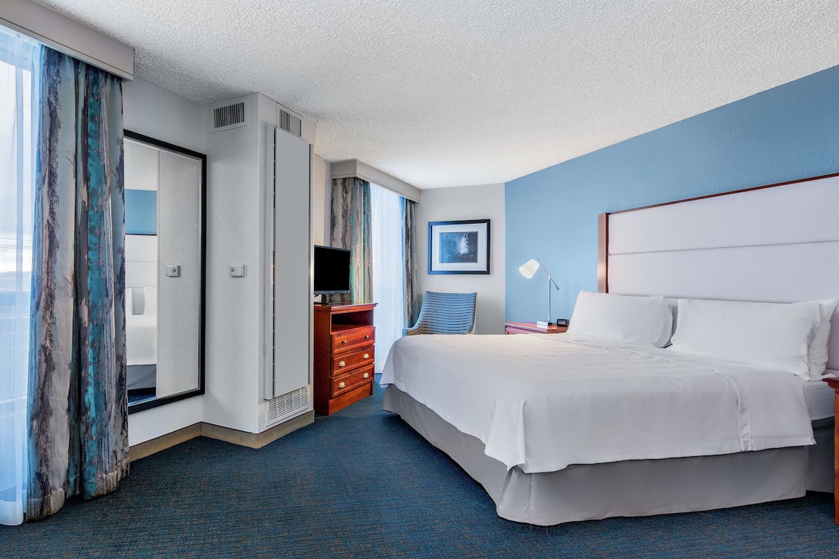 A hotel room with a large bed, a dresser, a TV, and a window with curtains.